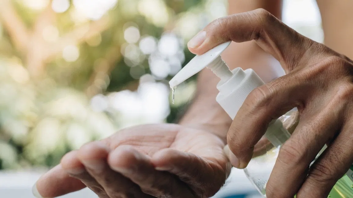 A closeup of a person applying hand sanitizer from a bottle onto the palm of their hands. 